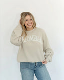 Girl wearing an oversized Chi Omega sorority sweatshirt in beige color with distressed arch CHI OMEGA across the front.